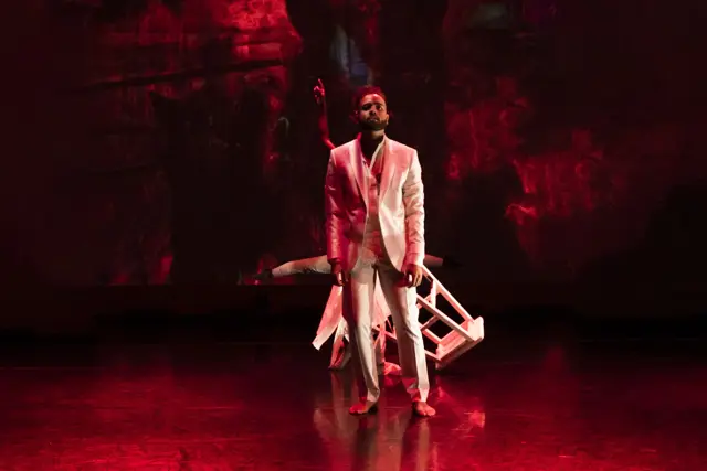 Curie Curie: a dancer in a white suit under red light, a stool tipped behind