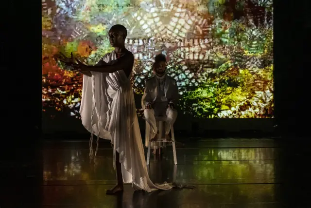 Curie Curie: two dancers before a projected lattice of gold and green light
