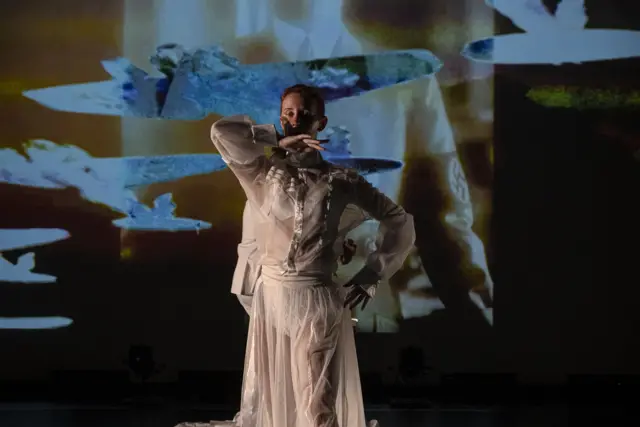 Curie Curie: a dancer in a white gown before a projection of flying white shapes