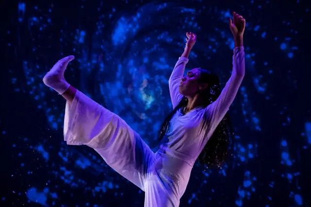 The Passage: a dancer kicking high before a projected blue starfield