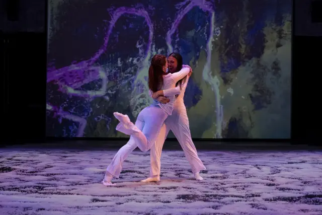 The Passage: two dancers embracing before projected violet trails