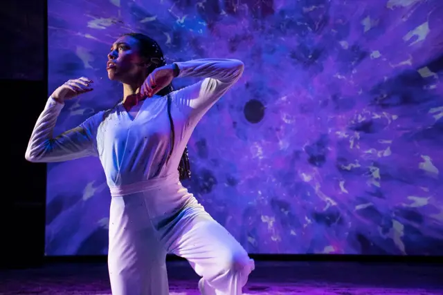The Passage: a dancer before a projected burst of violet shards