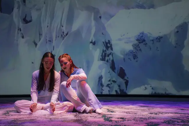 The Passage: two dancers seated on a snowy floor before projected mountains