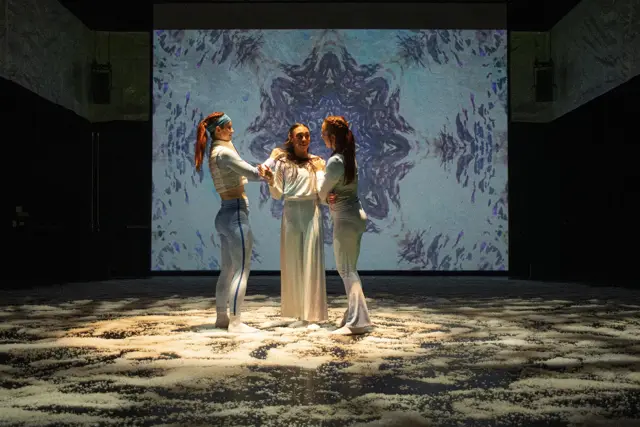 The Passage: three dancers in a pool of light before a projected snowflake pattern