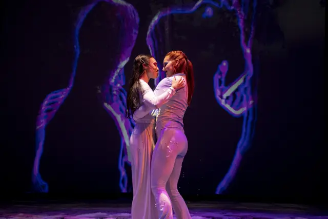 The Passage: two dancers before projected violet outlines of hands