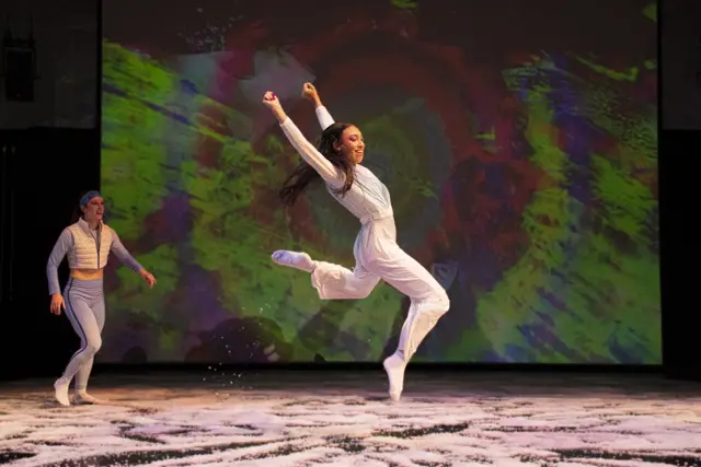 The Passage: a dancer leaping before a projected green and red swirl