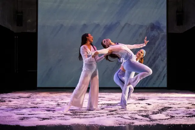 The Passage: three dancers in a lift on a snowy floor before projected gray light