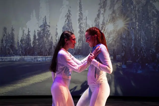 The Passage: two dancers face to face before a projected snowy forest with the sun breaking through
